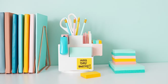 Un bureau avec des cahiers colorés, des crayons, des ciseaux et des notes Post-it®, créant un espace de travail organisé et confortable
