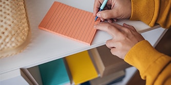 Une personne prenant des notes sur un note Post-it® lignée de couleur orange
